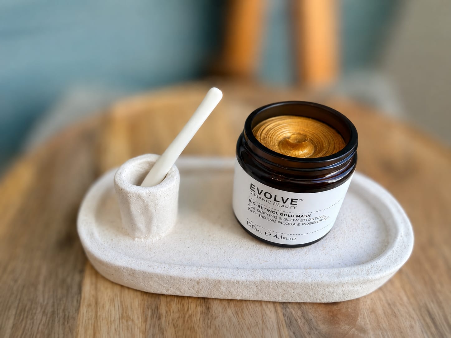 Een pot goudmasker van Evolve met een spatel op een stenen schaaltje